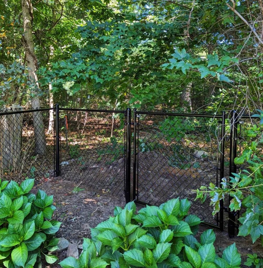 A black chain-link fence with a gate installed in a wooded area by Precision Fence NH in Hooksett, NH.