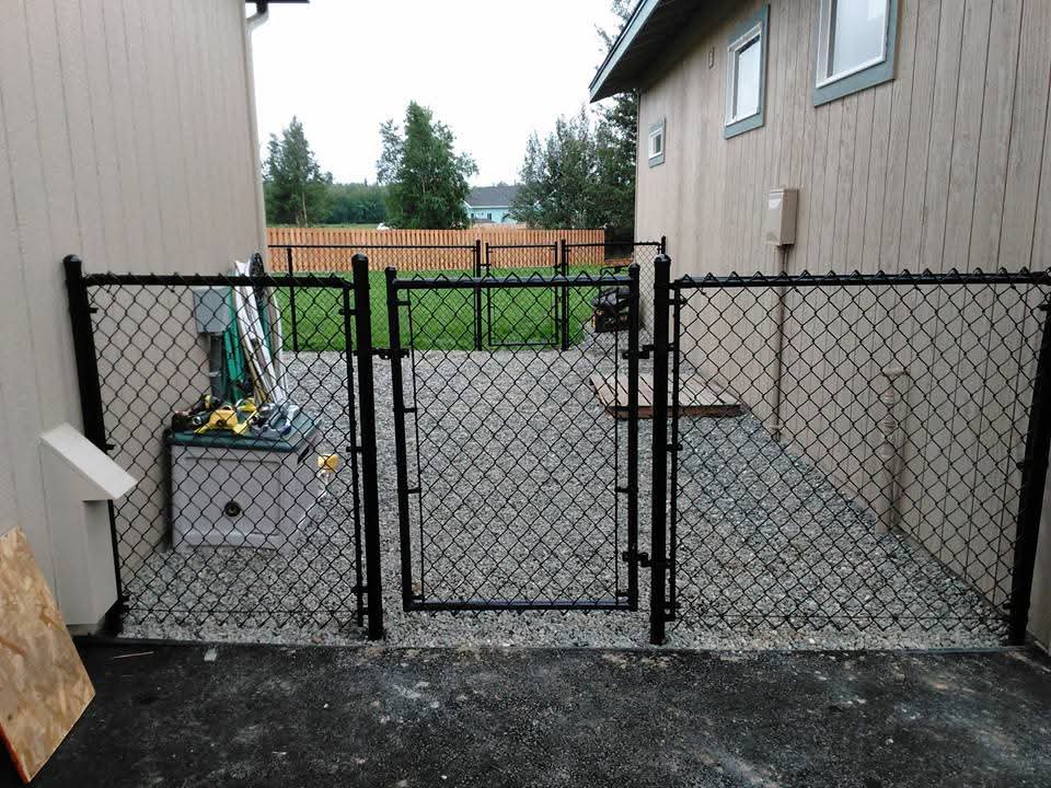 A newly installed black chain-link fence with two gates enclosing a gravel area, by Five Star Fence Co. in Anchorage, AK.