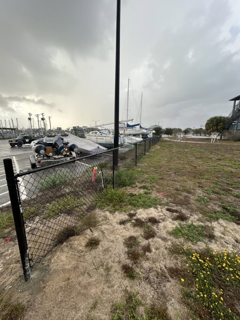 A newly installed black chain-link fence securing a property near a marina by C&F Solutions LLC in Gulfport, MS