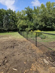 A newly installed black chain-link fence extending across a grassy property by JM Fence Works in Davenport, IA.