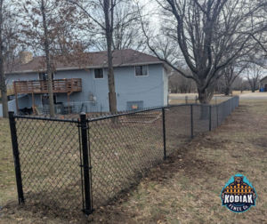 A newly installed black chain-link fence by Kodiak Fence Co. in Flower Mound, TX, bordering a backyard.