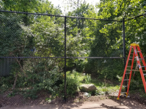 A black chain-link fence installation in progress with a ladder nearby, by Fox Fence Enterprises Inc in Clifton, NJ.