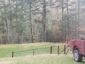 A newly installed black chain-link fence in a residential backyard, completed by MH Fence in Weare, NH.