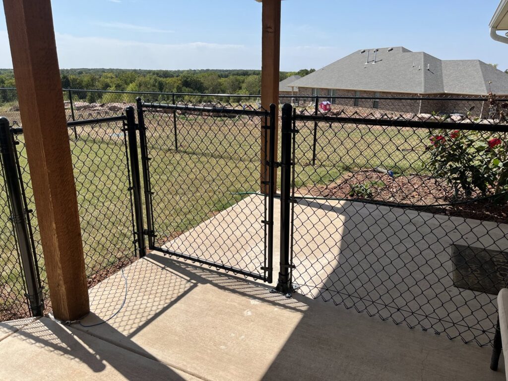 A black chain link fence with a gate enclosing a patio area, installed by 12 Corners Fence Company in Tecumseh, OK