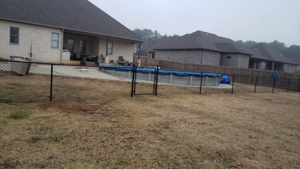 A black chain-link fence with a gate enclosing a pool area by Fences & Landscape Inc in Little Rock, AR.