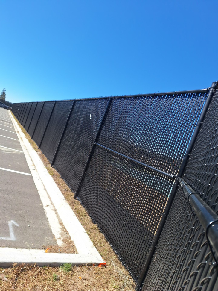 A black chain-link fence with privacy slats running alongside a parking lot, installed by First Fence of Georgia in Kennesaw, GA.