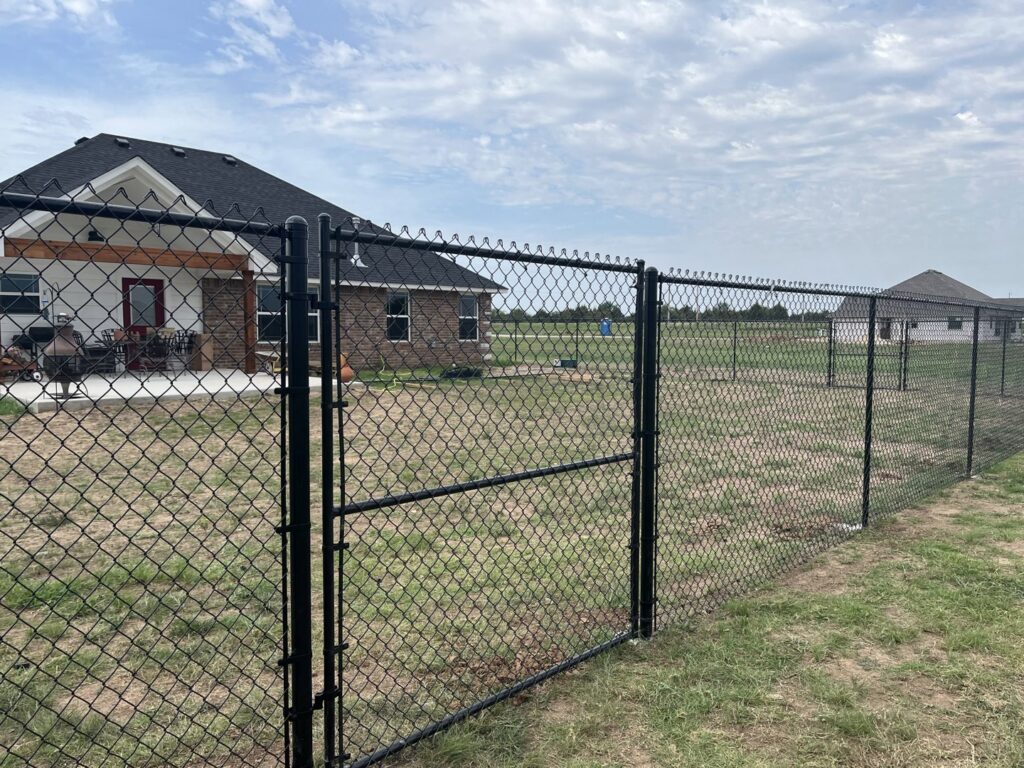 A newly installed black chain link fence enclosing a residential backyard by 12 Corners Fence Company in Tecumseh, OK
