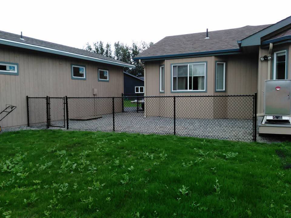 A new black chain-link fence with gates installed between residential homes, by Five Star Fence Co. in Anchorage, AK.