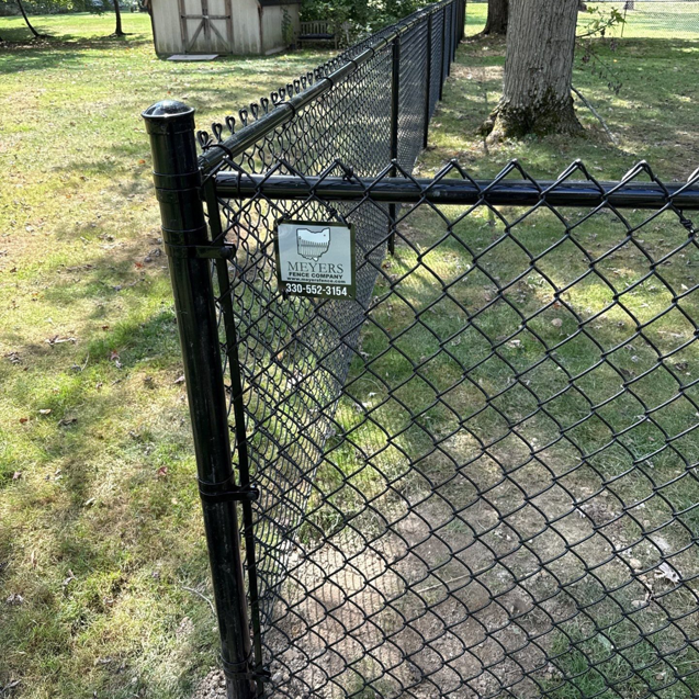 A newly installed black chain-link fence by Meyers Fence Company in a residential backyard in Kent, OH