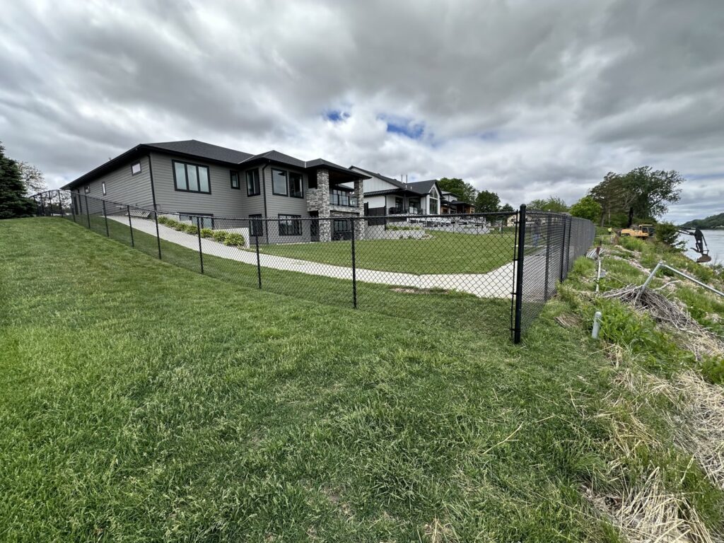 A black chain link fence installed along a sloped residential property by Bostwick Fencing, LLC in Sioux City, IA.