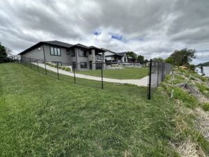 A black chain link fence installed along a sloped residential property by Bostwick Fencing, LLC in Sioux City, IA.