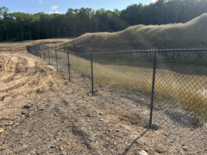 A black chain-link fence expertly installed on sloped terrain next to a pond by Alabama Fence & Rail LLC in Birmingham, AL.