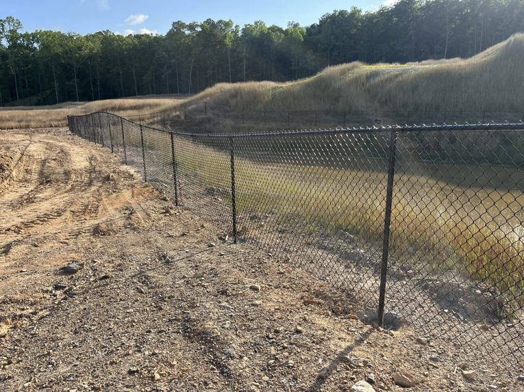 A black chain-link fence expertly installed on sloped terrain next to a pond by Alabama Fence & Rail LLC in Birmingham, AL.
