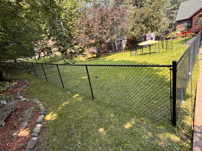 A newly installed black chain-link fence along a sloped backyard by 218 Fencing in Duluth, MN.