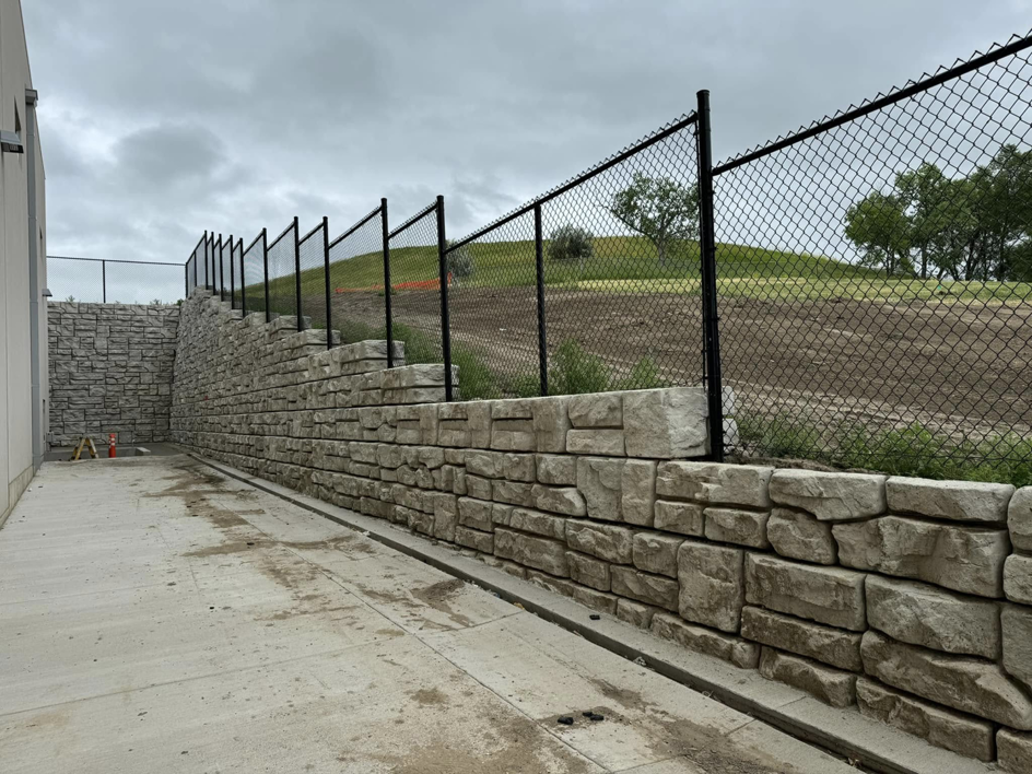 Black chain-link fence installed on top of a stone retaining wall by Solid Fence Co. in Sioux Falls, SD.