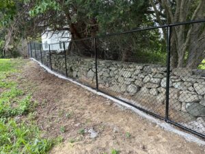 A black chain-link fence installed along a stone wall by Fence Pros Direct in Saunderstown, RI.