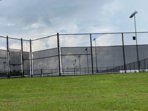 A black chain link fence with privacy screens surrounding a tennis court, installed by National Fence Services, LLC in Macon, GA.