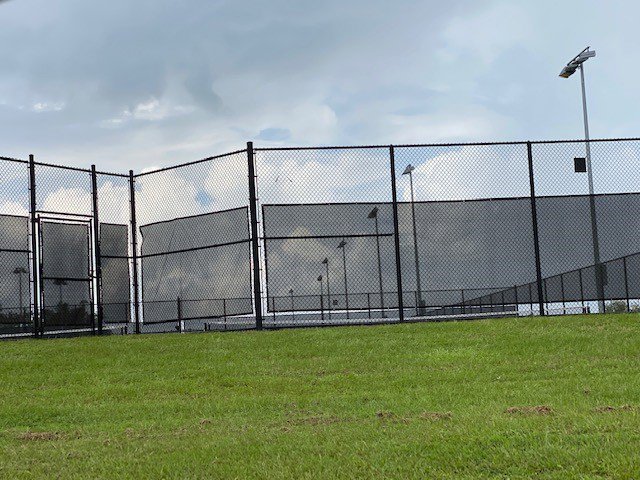 A black chain link fence with privacy screens surrounding a tennis court, installed by National Fence Services, LLC in Macon, GA.