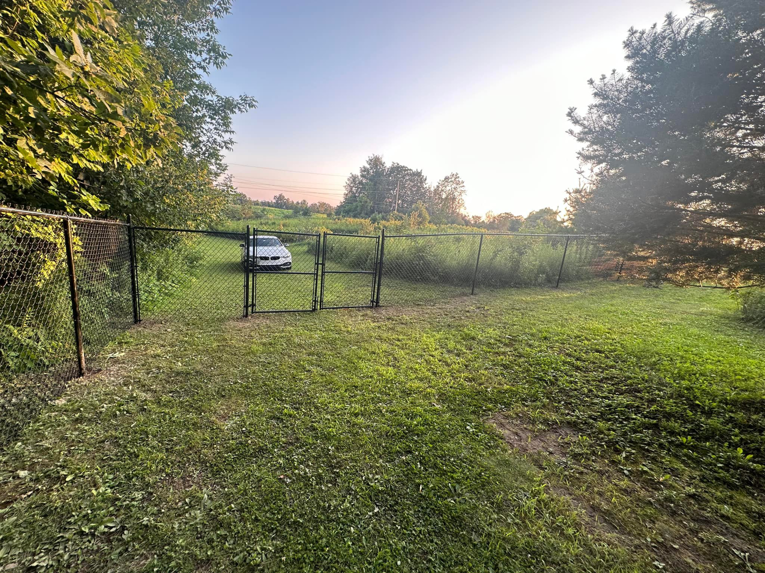 A newly installed black chain-link fence with a double gate in a spacious outdoor area by Fenced Up, LLC in Ravena, NY.
