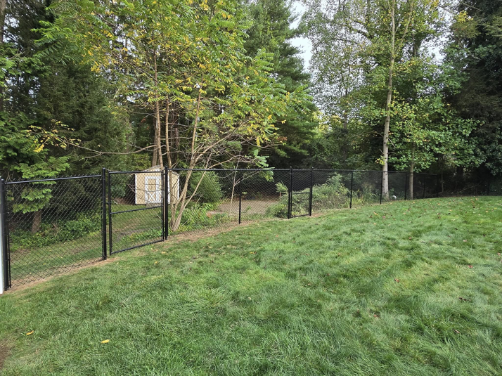 A black chain-link fence with a gate installed on a sloped grassy area by Homestead Fence in Cumberland, RI.