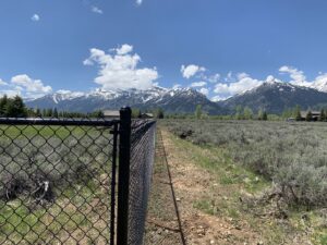 A black chain-link fence installed in a rural setting with scenic mountains in the background by Idaho Falls Fencing in Idaho Falls, ID.