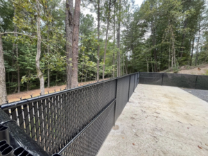 A newly installed black chain-link fence along a concrete path in a wooded area by Alabama Fence & Rail LLC in Birmingham, AL.