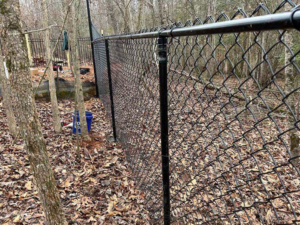 A newly installed black chain-link fence in a wooded residential area by FenceMax in Spartanburg, SC