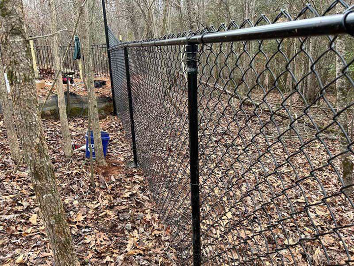A newly installed black chain-link fence in a wooded residential area by FenceMax in Spartanburg, SC