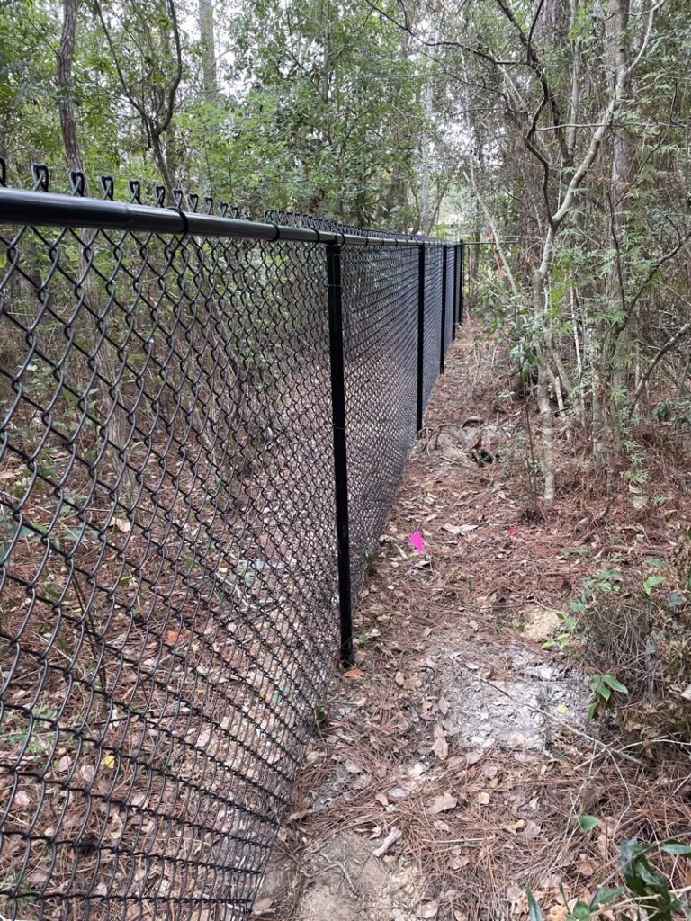 A black chain-link fence installed through a wooded area by Jaguar Fence LLC in Mobile, AL.