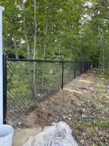A newly installed black chain-link fence running through a wooded area by Texeira Fencing & Concrete in Springfield, MA.