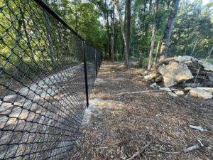A close-up view of a black chain-link fence installed along a path in a wooded area by Alabama Fence & Rail LLC in Birmingham, AL.