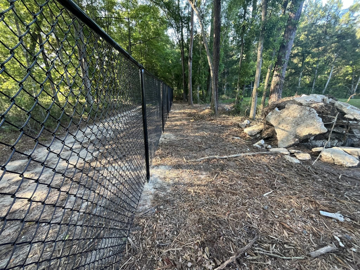 A close-up view of a black chain-link fence installed along a path in a wooded area by Alabama Fence & Rail LLC in Birmingham, AL.