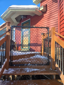 A newly installed black chain link gate on a wooden deck staircase by Dore's Fence Company in Greenbush, ME.