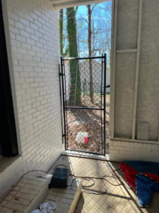 A black chain-link walk-through gate installed next to a brick wall by Allen Fences & Decks, LLC in Tuscaloosa, AL.