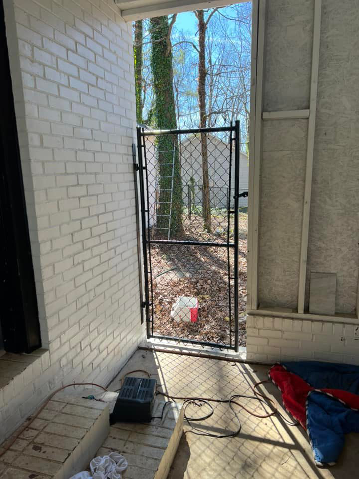 A black chain-link walk-through gate installed next to a brick wall by Allen Fences & Decks, LLC in Tuscaloosa, AL.