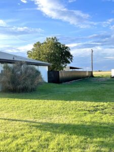 A long black corrugated metal fence extending across a sunny landscape, installed by DC Fencing LLC in Clovis, NM.