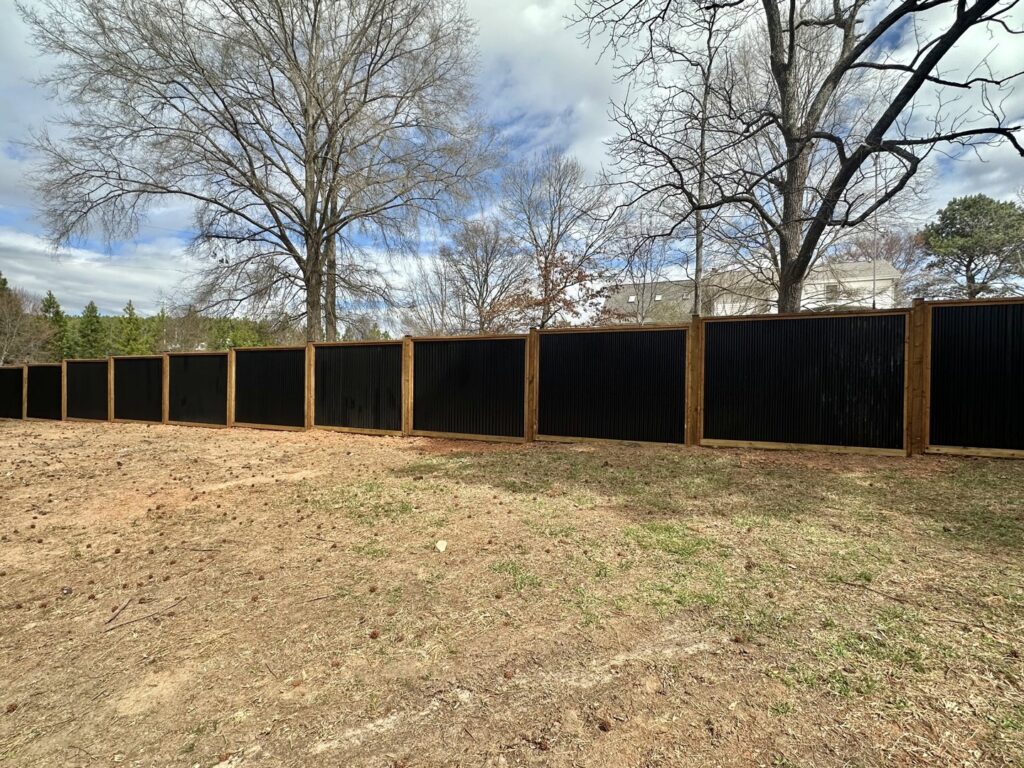 A modern black corrugated metal privacy fence with wooden posts, expertly installed by Cavitt Fencing in Concord, NC.