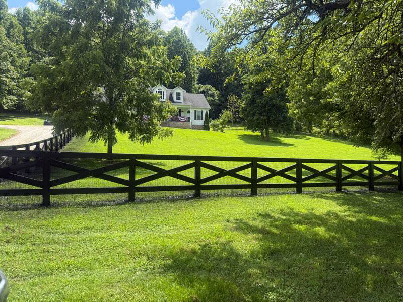 A black cross-buck wooden fence with wire mesh installed in front of a residential property by The Fence Painter in Lynnville, TN.
