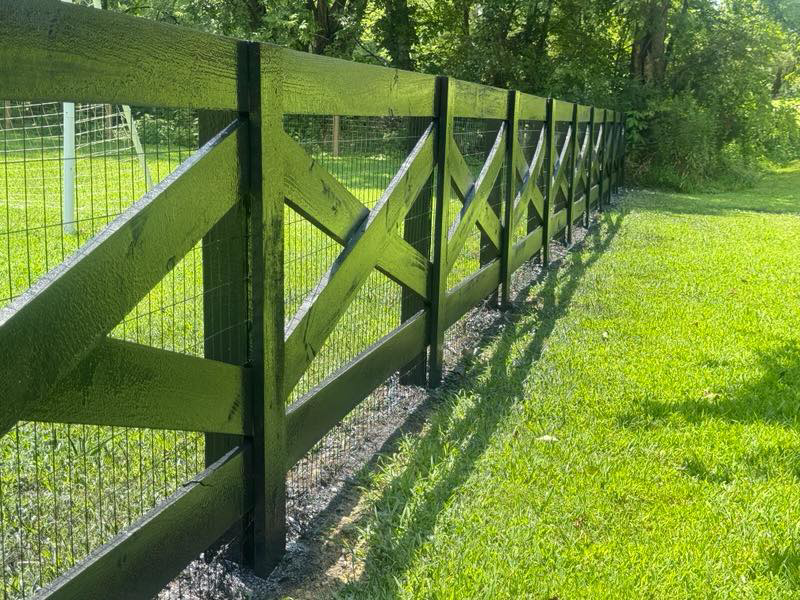 A close-up of a black cross-buck wooden fence with wire mesh installed by The Fence Painter in Lynnville, TN.