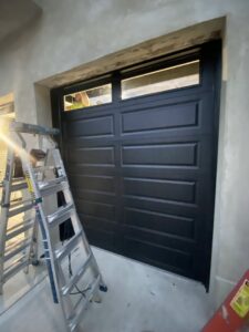 A black garage door with windows, and a ladder nearby, indicating installation by The Region's Garage Door Repair in Hammond, IN.