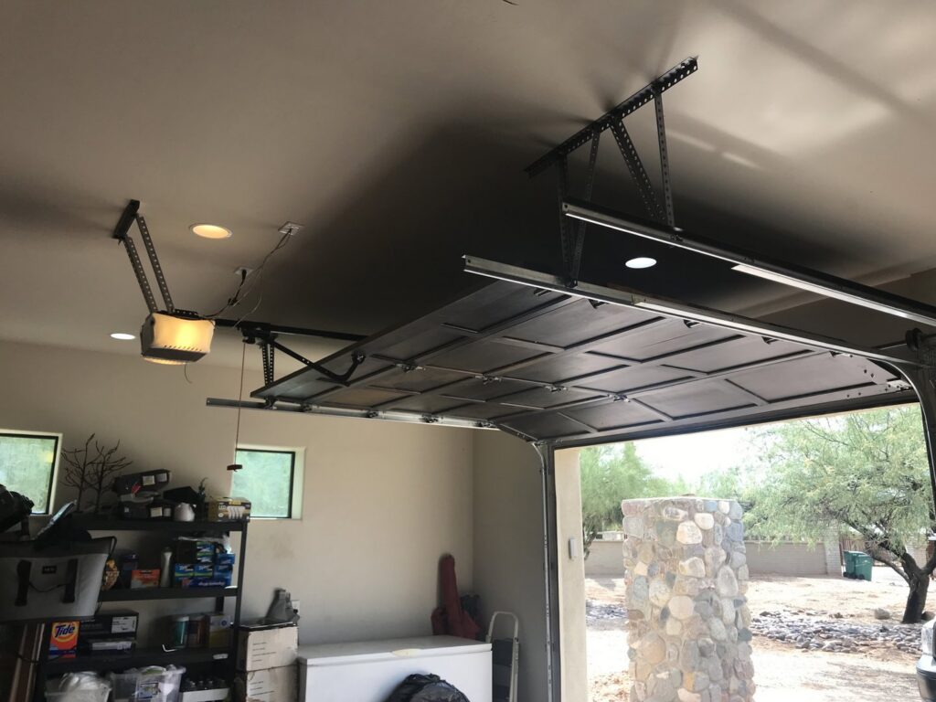 An interior view of a garage showing the mechanism and opener for a black garage door, installed by Johns Garage Doors in Tucson, AZ.