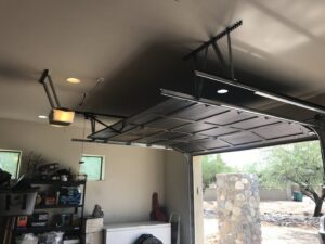 An interior view of a garage showing the mechanism and opener for a black garage door, installed by Johns Garage Doors in Tucson, AZ.