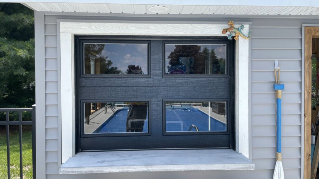 Black garage door installed as a pass-through bar window overlooking a pool by Superior Overhead Door, LLC in Granger, IN