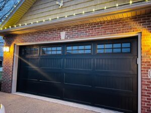 A black garage door with decorative windows on a brick house, installed by A+ Garage Door Repair in Evansville, IN.