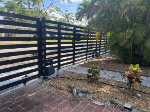 A long black horizontal slat fence with an automatic gate opener installed by Miami Fence Installation Contractors in Miami, FL.