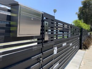 A modern black horizontal slat fence with an integrated mailbox and intercom system, installed by Harwell Fencing & Gates Inc. in Los Angeles, CA.