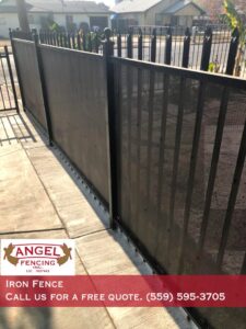 A black iron fence with privacy screens along a sidewalk installed by Angel Fencing Inc. in Fresno, CA