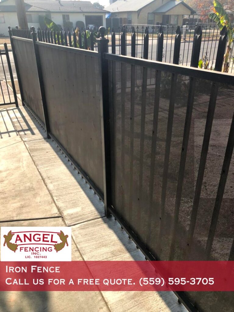 A black iron fence with privacy screens along a sidewalk installed by Angel Fencing Inc. in Fresno, CA