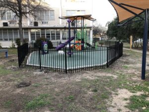A black iron fence enclosing a children's playground for safety, installed by Superior Fence Co. of San Antonio, TX.