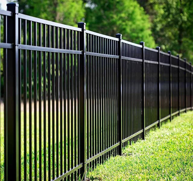 A long black metal or aluminum fence installed in a green lawn by Vanguard Fencing LLC in Lenexa, KS.